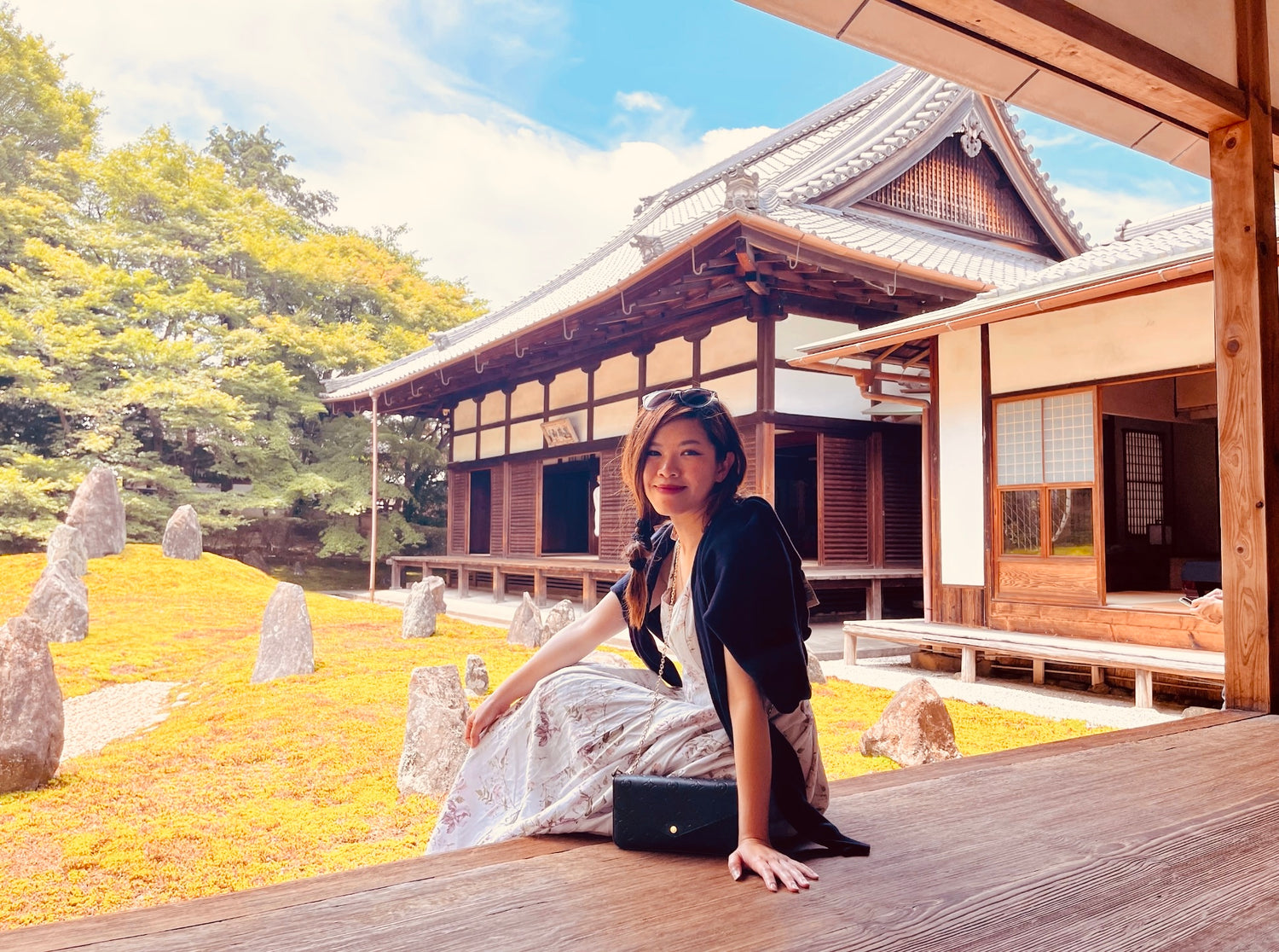 Woman sitting on a wooden platform in front of a traditional Japanese building with stone lanterns.