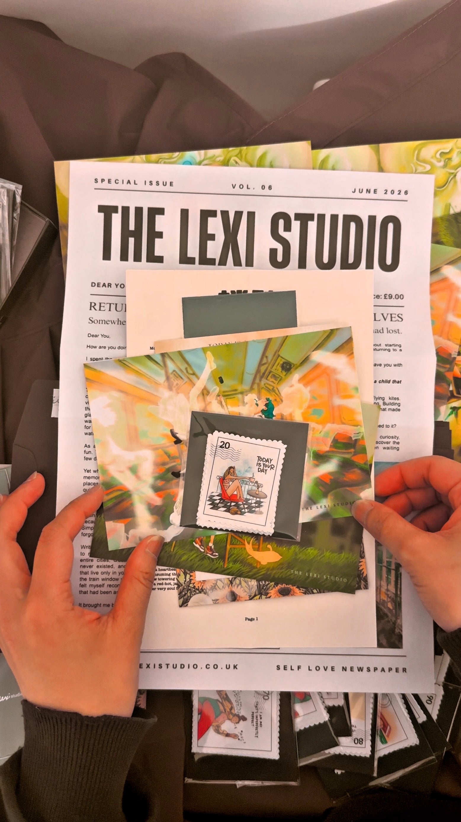 Person holding a magazine titled 'The Lexi Studio' with colorful design on a blurred background
